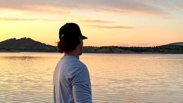 A person fishing by a calm body of water during sunset.