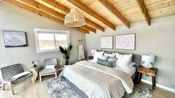 A bedroom with a large bed, a wooden ceiling, a window, and a bedside table.