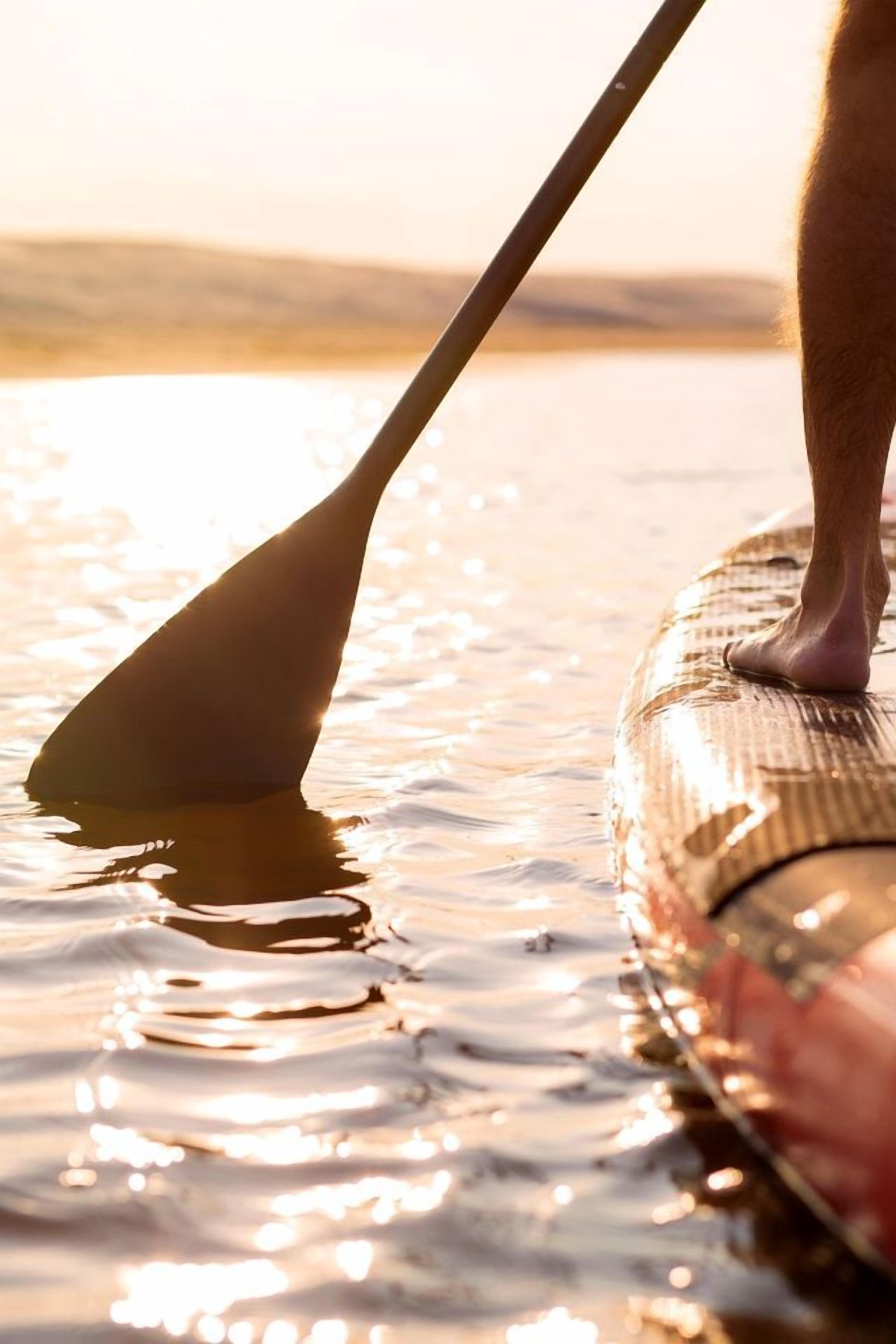 A person standing on a paddleboard in calm water.