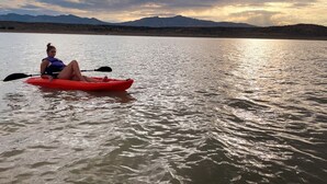Une personne pratiquant le kayak sur une étendue d’eau calme, avec des montagnes en arrière-plan.