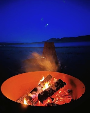 A campfire in a circular fire pit with a view of a mountain range under a night sky.