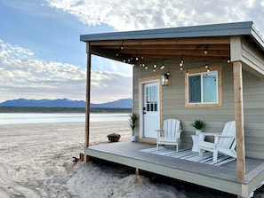 A beach house with a porch, two chairs, a table, and a potted plant.