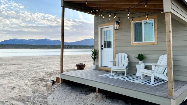 A beach house with a porch, two chairs, a table, and a potted plant.