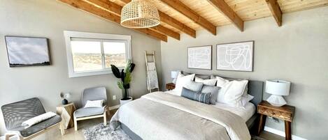 Un dormitorio con una cama grande, techo de madera, una ventana y una mesita de noche.