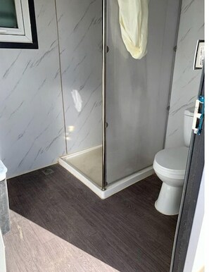A bathroom with a shower enclosure, a toilet, and a marble-patterned wall.
