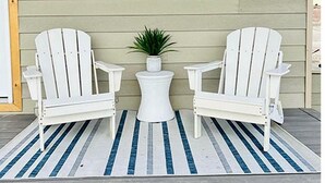 Une véranda avec deux fauteuils Adirondack blancs, une petite table blanche et une plante en pot.