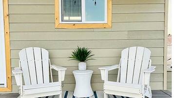 A porch with two white Adirondack chairs, a small white table, and a potted plant.