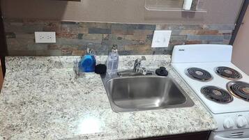 A kitchen with granite countertops, a stainless steel sink, a white Danby stove, and a stone backsplash.