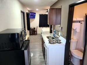A compact kitchen with a microwave, sink, and cabinets, leading to a bathroom with a toilet and shower. - Quiet Adventure Base with BBQ Area & Scenic Nights in Williams, Arizona (Williams)