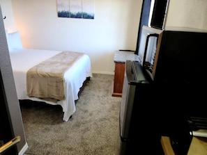 Un dormitorio con cama, televisión y refrigerador.