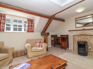 A cozy living room with a fireplace, a sofa, a wooden coffee table, and a window with plaid curtains. - The Old Stables (Gloucester)