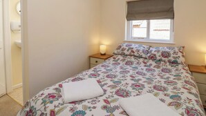 Ein Schlafzimmer mit Bett, Fenster mit Jalousie, Nachttisch mit Lampe und einer Tür zu einem Badezimmer.