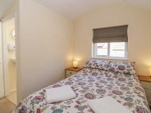 Ein Schlafzimmer mit Bett, Fenster mit Jalousie, Nachttisch mit Lampe und einer Tür zu einem Badezimmer.