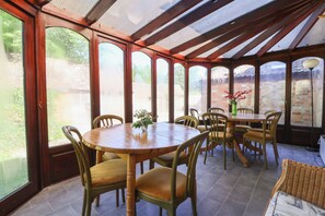 A sunroom with a wooden table and chairs, large windows, and a brick wall. - The Old Stables (Gloucester)
