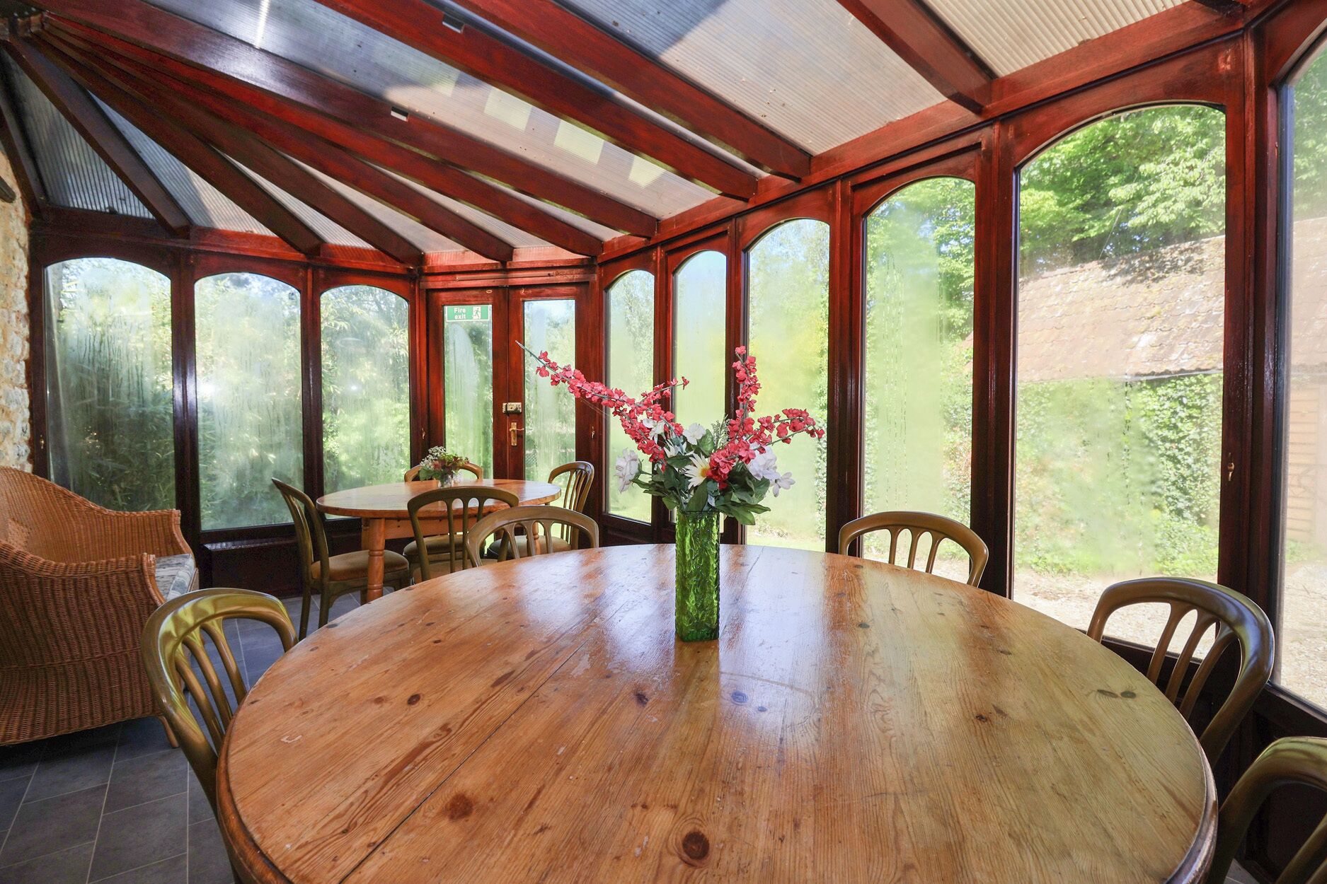A covered dining area with a round wooden table, chairs, and a vase with flowers.