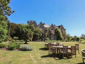 A large stone building with multiple windows and a lawn with wooden tables and chairs. - The Old Stables (Gloucester)