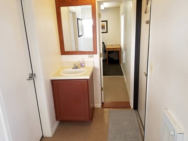 Ein schmales Dünnwandzimmer, das zu einem Badezimmer mit Waschbecken, Spiegel und Schrank führt.