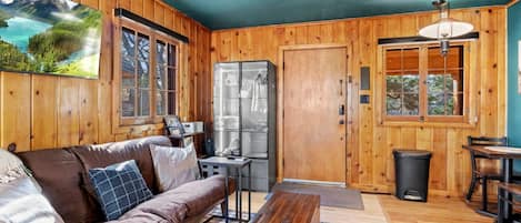 Una habitación acogedora con detalles de madera, un sofá, una mesa, un refrigerador y una ventana con vistas a las montañas.