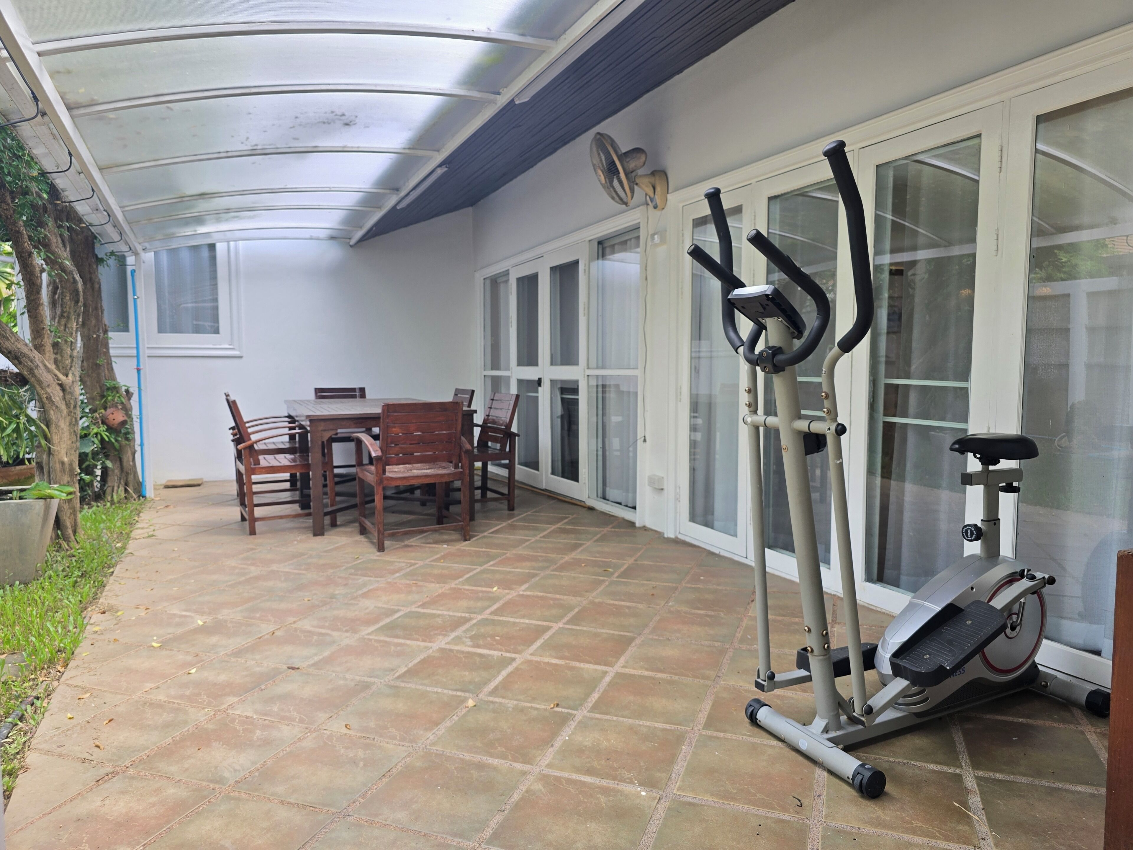 A covered patio area with a table and chairs, exercise equipment, and a view of the outside.