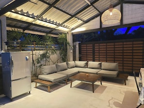 A covered outdoor seating area with a sofa, a coffee table, and a refrigerator. - Spacious 5-bedroom house with private pool in Jed yod Chiang Mai 5min to Nimman (Chang Wat Chiang Mai)