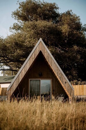 A wooden cabin with a triangular roof, a large window, and a door. - Unique A-Frame Cabin Stay with Shared Bathhouse & Scenic Outdoor Space in Emigrant, Montana (Emigrant)