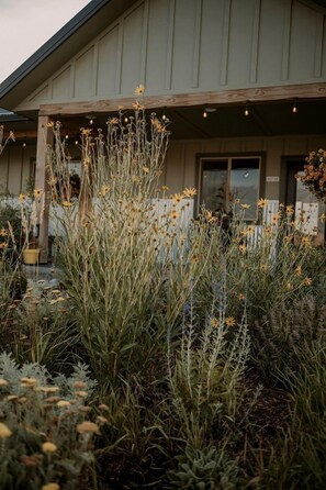 A building with a covered outdoor area featuring tall grasses and wildflowers. - Unique A-Frame Cabin Stay with Shared Bathhouse & Scenic Outdoor Space in Emigrant, Montana (Emigrant)