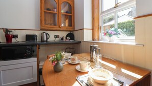 A kitchen with wooden cabinets, a microwave, a kettle, and a window with a view of a car and greenery. - Harness Rooms (Gloucester)