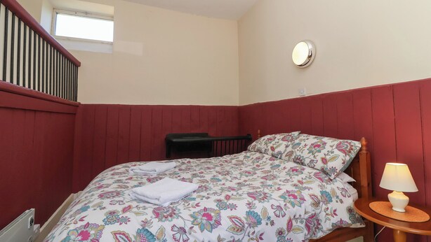 A bedroom with a bed, a nightstand, a window, and a red wall. - Harness Rooms (Gloucester)