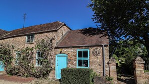 A traditional brick house with a blue door, a visible clock, and a small garden area. - Harness Rooms (Gloucester)