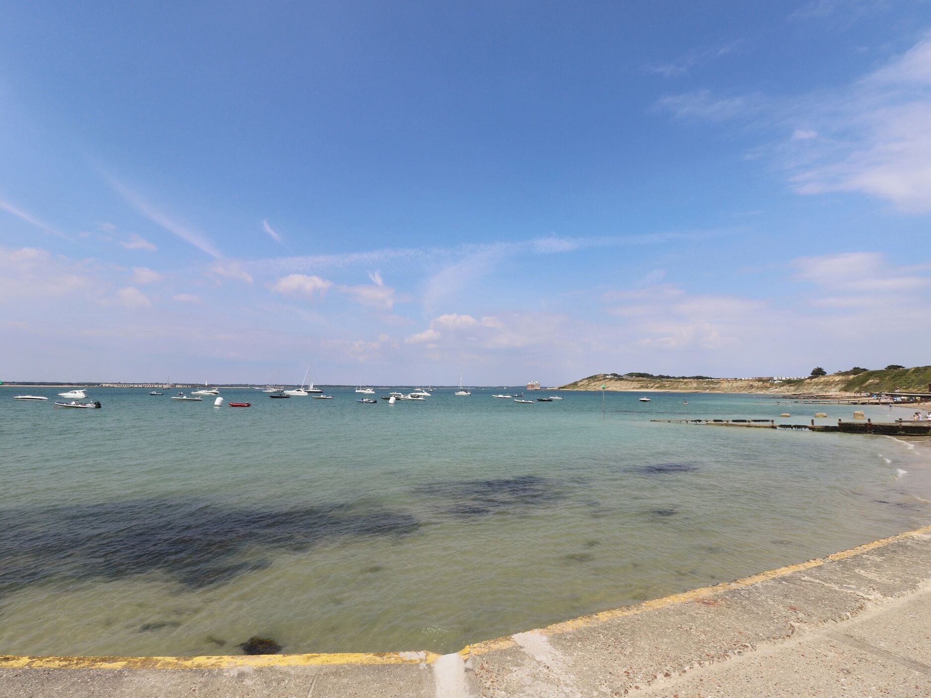 Eine Küstenlandschaft mit Booten, klarem Wasser und einem Sandstrand.