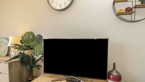 Una sala de estar moderna con un televisor de pantalla plana sobre una mesa de madera, un reloj de pared, una planta en maceta y un jarrón decorativo.