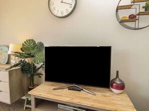 Ein modernes Wohnzimmer mit einem Flachbildfernseher auf einem Holztisch, einer Wanduhr, einer Topfpflanze und einer dekorativen Vase.