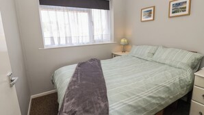Un dormitorio con cama, ventana con cortinas, lámpara de noche y dos cuadros en la pared.