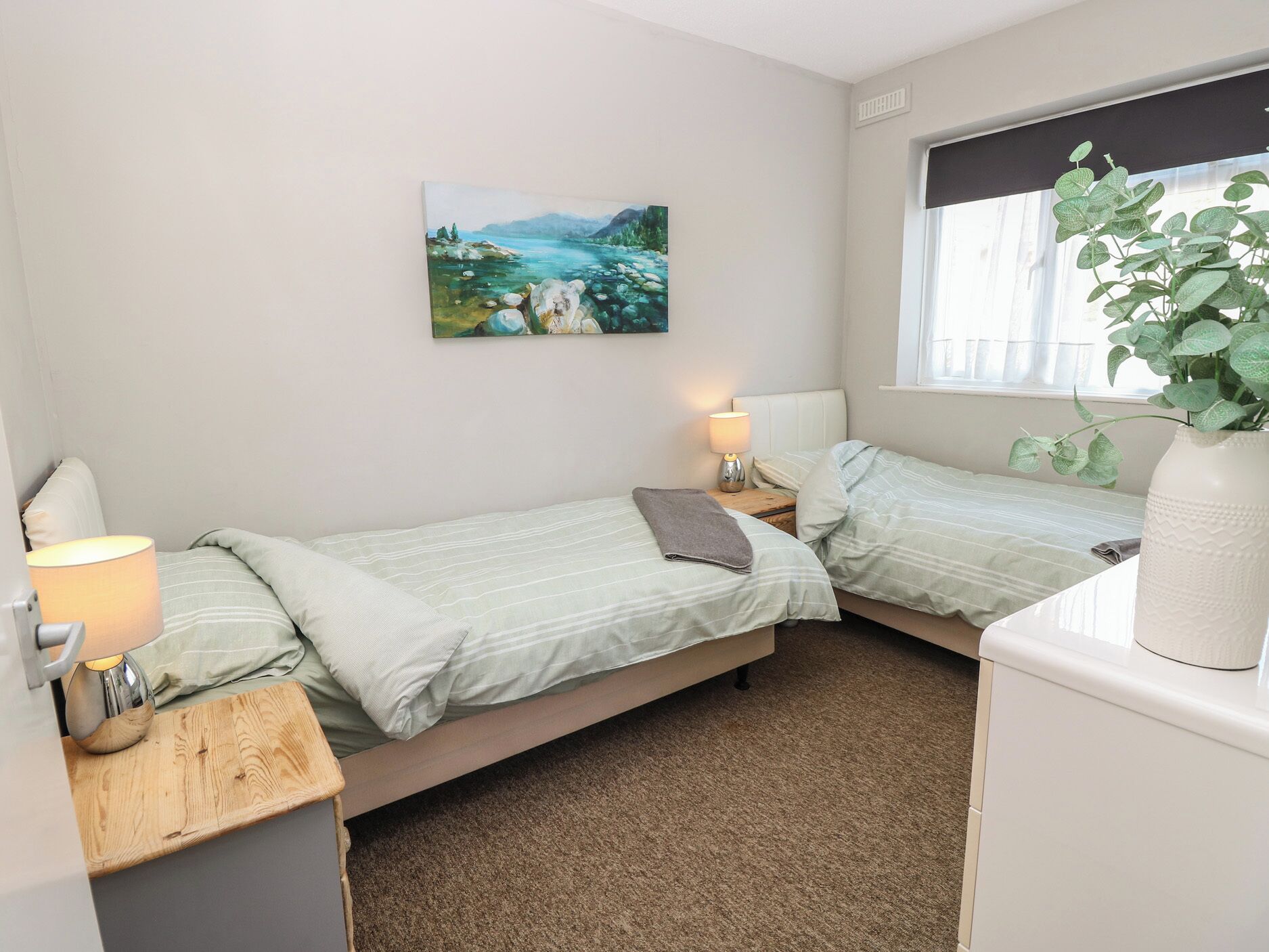 Ein Schlafzimmer mit zwei Betten, einem Fenster mit Blick, einem Bild an der Wand und einer Pflanze auf einem Tisch.