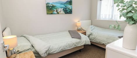 A bedroom with two beds, a window with a view, a painting on the wall, and a plant on a table.