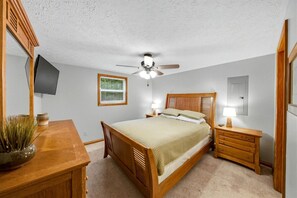 A bedroom with a bed, bedside tables, a ceiling fan, a TV mounted on the wall, and a window. - Lakefront Cabin with Hot-tub and Dock in Tennessee (Speedwell)