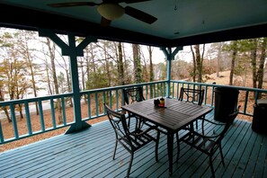Eine überdachte Terrasse im Freien mit Tisch und Stühlen, umgeben von einem Geländer, mit Blick auf ein bewaldetes Gebiet.
