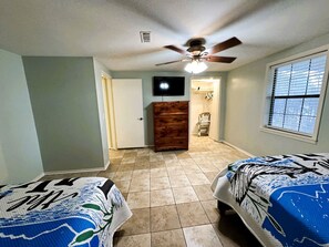Ein Schlafzimmer mit zwei Betten, einem Deckenventilator, einem Fernseher und einem Fenster.