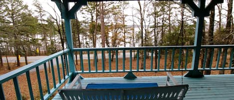 Une véranda avec un banc, une balustrade et une vue sur les arbres et une route.