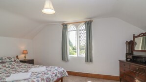 Een slaapkamer met een bed, een kaptafel, een raam met gordijnen, een lamp en een plafondlamp.