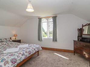 Une chambre à coucher avec un lit, une commode, une fenêtre avec des rideaux, une lampe et un luminaire au plafond.