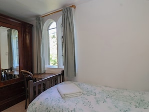 Ein Schlafzimmer mit Bett, Schreibtisch, Stuhl, Spiegel und einem Fenster mit Vorhängen.