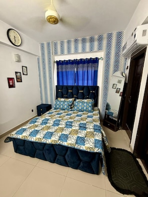 A bedroom with a bed, a bedside table, a wall clock, and a door. - 1BR Cozy Apartment, Diamond Mall and Residencia, Gulberg Greens (Islamabad)