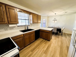 A kitchen with wooden cabinets, a black sink, and a dining area with a table and chairs.