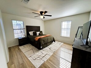 Un dormitorio con cama, mesitas de noche, ventilador de techo, televisión y ventana con persianas.