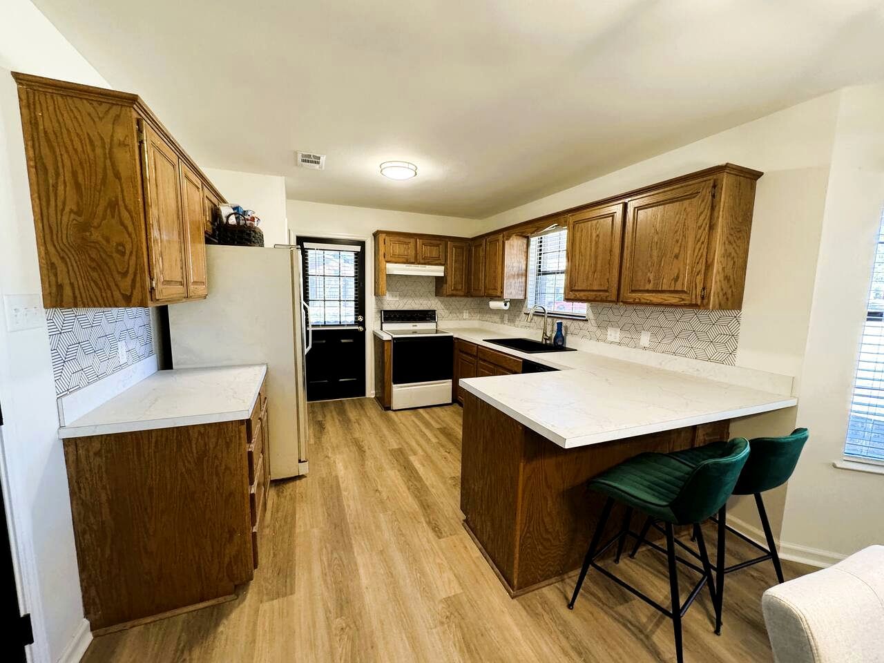 A modern kitchen with wooden cabinets, a central island with bar stools, and a built-in oven.