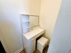 Un baño pequeño y blanco, cerrado, con tocador, espejo y banco.