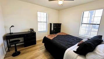 A bedroom with a bed, a desk, a chair, a dresser, and a ceiling fan.