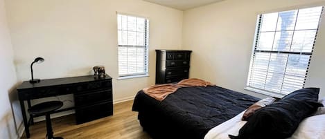 A bedroom with a bed, a desk, a chair, a dresser, and a ceiling fan.