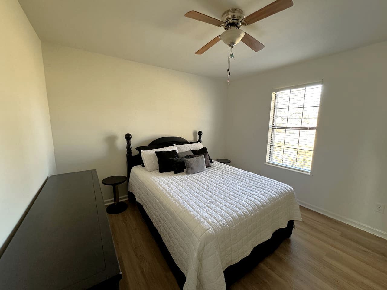 Une chambre à coucher avec un lit, un ventilateur de plafond, une fenêtre et une petite table.